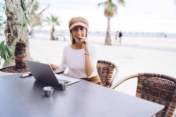 모자를 여성이 카페에서 쉬면서 노트북으로 원격으로 일하고 올리브를 맛보는 — 스톡 사진