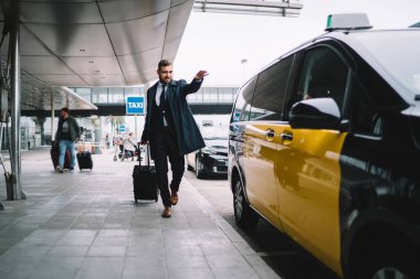 Sarı taksiye el sallayan yakışıklı erkek yolcu seyahat sırasında iş toplantısına acele et, valizli Kafkasyalı avukat havaalanı dışından taksi çağırıyor.