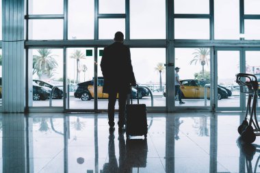 İş seyahatinden sonra gelen valizli erkek yolcunun arka görüntüsü, bagajlı pilot silueti iş çıkışı için nakil aracını bekliyor.