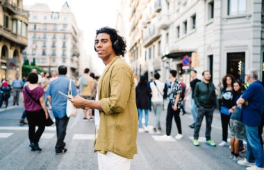Kalabalık caddelerde yürürken günlük giysiler ve kulaklıklar takıp müzik dinleyen genç, pozitif erkek yaya görüntüsü