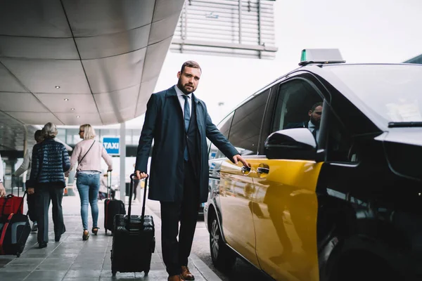空港からタクシーですぐの正式な服を着た30歳の白人ビジネスマンの完全な長さの肖像 タクシー近くのカメラを見て荷物スーツケースを持つ自信のある男性誇り高いCeo — ストック写真