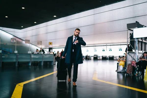 現代のスマートウォッチの白人ビジネスマンチェック時間はターミナルの空港ゲートに急いで 仕事旅行中にウェアラブル腕時計を使用して荷物スーツケースと正式に服を着た通勤者 — ストック写真
