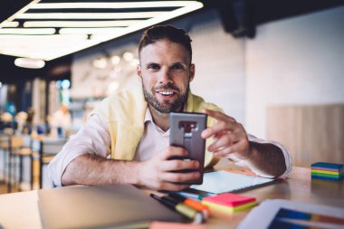 Akıllı gündelik giyinen başarılı erkek girişimcilerin yarısı teneffüste kameraya gülümseyip modern dijital tablet, akıllı telefon ve dokunmatik ped ile çalışan neşeli serbest yazar.