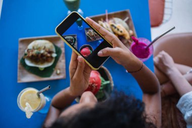 Kesilmiş kadın vlogcu cep telefonu ana kamerasıyla medya fotoğraflarına tıklıyor ve yemek bloguna paylaşım için içerik yaratıyor, gurme öğle yemeği sırasında Latin bistro kafede Meksika yemeklerini fotoğraflıyor