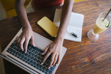 Uzaktan kumandalı bir projede çalışan, elinde meyve suyu ve defter bulunan tahtadan bir masada oturan...