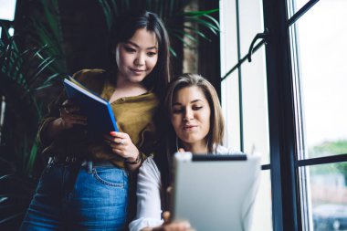 Modern çalışma ortamında proje üzerinde çalışırken tablet kullanan gündelik giysiler içindeki kadın meslektaşların düşük açılı görüntüsü