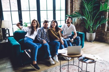 Çağdaş ofiste rahat koltukta oturup selfie çeken çok ırklı neşeli iş arkadaşlarıyla dolu bir vücut.