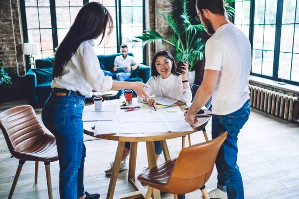 Beyaz tişörtlü, çok ırklı meslektaşlar gazetelerle çalışırken iş stratejisi hakkında konuşuyor ve ofiste kahve içmenin keyfini çıkarıyor.