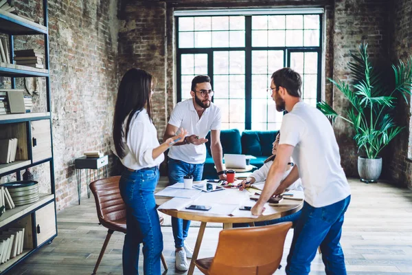 Bir grup meslektaş, büyük pencereli modern projenin yaratıcı fikirleri üzerinde kafa patlatırken ayakta ve oturuyorlar.