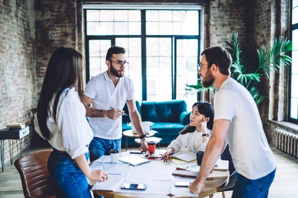 Çok ırklı genç meslektaşlardan oluşan bir ekip gündelik kıyafetlerle masa başında akıllı telefonlar ve modern çalışma alanlarında hazır fincanlarla beyin fırtınası yapıyor.