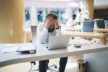 Fazla çalışan erkek çalışanın çalışma sürecinde baş ağrısı çekmesi problemler hakkında strese girmesi, üzgün depresif adamın iş yerinde dizüstü bilgisayarla hayal kırıklığına uğraması sorunlardan bıkması.