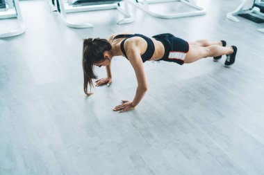 Çağdaş hafif spor salonunda yerde şınav egzersizi yapan, aktif giyimli, zayıf yüzlü, sporcu kadın.