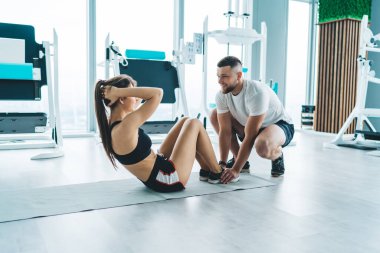 Kadın vücudunun bütünü, yattığı yerden gövdesini kaldırırken el ele tutuşuyor ve alt bacakları tutan pozitif antrenör.