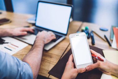 Anonim adam boş ekranlı dizüstü bilgisayar kullanıyor ve kadın meslektaşı ofiste birlikte otururken akıllı telefondan mesaj yazıyor.