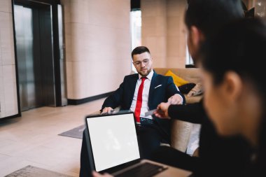 Bir grup ciddi iş arkadaşı modern ofiste dizüstü bilgisayarla oturup toplantı sırasında iş projesi fikirlerini tartışıyor.