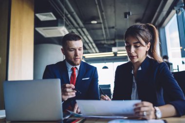 Beyaz erkek ve kadın iş adamları masa başında dijital pazarlama için modern teknolojiyle oturuyorlar ve ofiste beyin fırtınası sırasında takas sözleşmelerini tartışıyorlar.