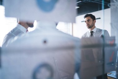 Resmi olarak odaklanmış genç işadamları fikirleri ve çalışma planını tartışırken aynı zamanda cam duvarın arkasında modern yaratıcı ofis çalışma alanına sıkışmış kağıtlarla dikiliyorlar.