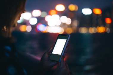 Plastik çantada cep telefonu kullanan tanınmayan bir kadın. Uygulama, gece nehri ve Bokeh şehir ışıklarının bulanık arka planında sahte.