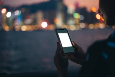 Plastik çantada modern telefon aygıtı kullanan tanınmayan bir kadın. Uygulama, gece nehri ve Bokeh şehir ışıklarının bulanık arka planında taklit yapıyor.