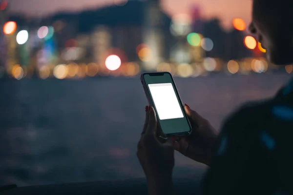 作物認識できない女性は夜の川やボケの都市照明のぼやけた背景にアプリケーションモックアップとプラスチックケースで現代の携帯電話デバイスを使用して — ストック写真