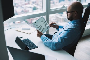 Tablet sörfü yaparken ve modern işyerinde çalışırken pencerenin yanındaki beyaz bilgisayar masasında oturan yüzü olmayan yöneticinin yan görüntüsü