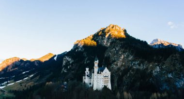 Güneş ışığı altındaki görkemli kayalık dağ manzarası. Dağ sırtında kozalaklı ağaçlarla dolu bayırdaki eski taş ortaçağ şatosu.