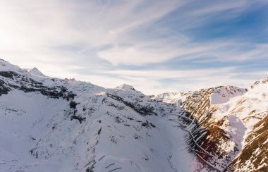Kışın güneşli bir günde mavi bulutlu gökyüzünün altındaki yüksek dağlık Alpler 'in yüksek karlı zirvelerinin drone görüntüsü