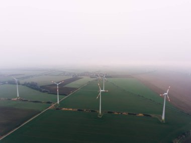 Elektrik üretimi için yel değirmenlerinin ve bulutlu bir günde sis kaplı Alplerdeki tarım alanlarının havadan görünüşü