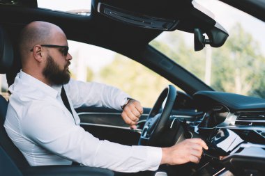 Otomobilde oturan ve modern bir aracı trafikte sürerken kol saatine bakan başarılı erkek patronun yan görüntüsü