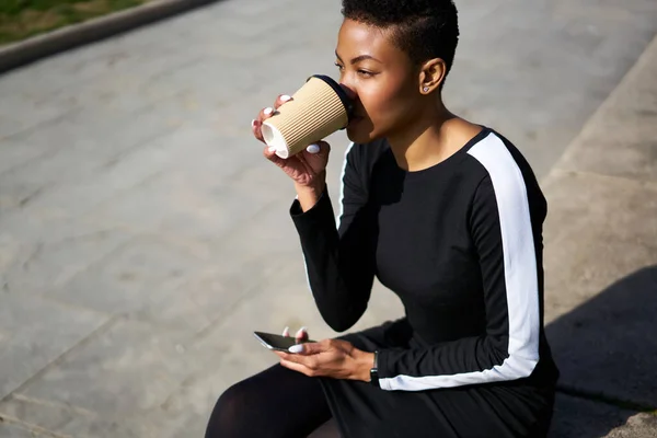 作物の高角度若いアフリカ系アメリカ人女性カジュアルな服を離れて見て スマートフォンで街の通りの石段に座っている間に行くためにコーヒーを飲む — ストック写真