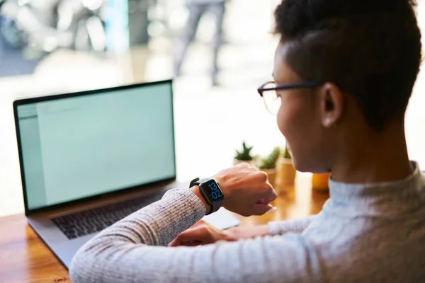 隐约可见的女性坐在木制桌旁 手持笔记本电脑 在咖啡店工作时在智能手表下检查时间 — 图库照片
