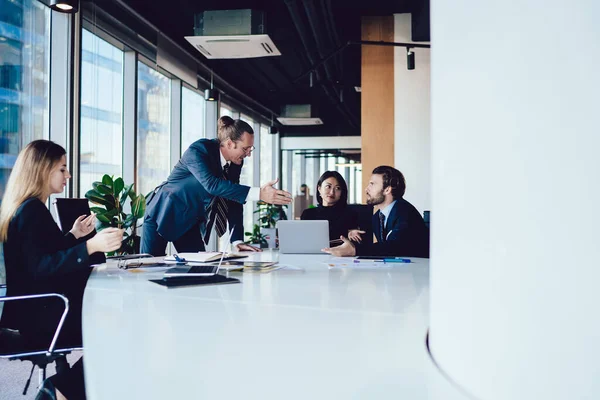 現代のライトオフィスの会議室でブリーフィングを受けながら テーブルに立って多様な従業員と話をするエグゼクティブ正式な男 — ストック写真