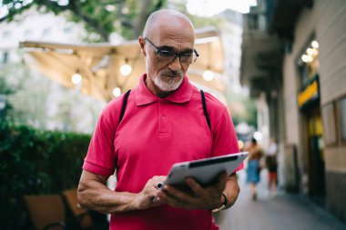 Çevrimiçi modda sohbet ve mesajlaşma için 4G 'ye bağlanan yaşlı blogcu, klasik gözlüklü son sınıf öğrencisi, kentte ayakta duran modern dokunmatik bloknotlardan e-posta aldı