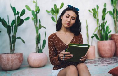 Ev verandasında oturmuş ev ödevini bitirdikten sonra not defterine bakan gündelik kıyafetli, düşünceli genç etnik kız öğrenci.