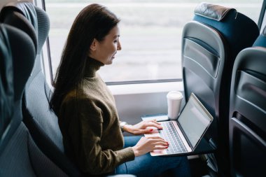 Neşeli Asyalı kadın dijital göçebe teknoloji ve araba yolculuğunda kablosuz bağlantı ile çalışıyor, gülümseyen kadın dizüstü bilgisayarda dizüstü bilgisayardan haberleri okuyarak trende mesafelere gidiyor.