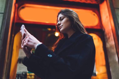 Resmi kıyafetli, gözlüklü, akıllı telefonlu ciddi bir kadının yürüme sırasında pencerenin yanında dikilirken...