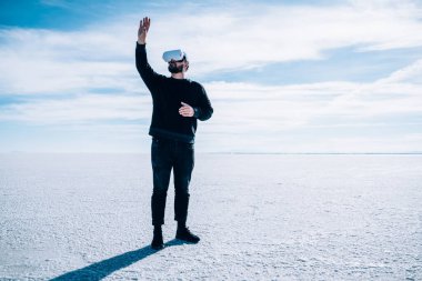 Sanal gerçeklik gözlüğü kullanarak Bonneville Tuz Düzlükleri 'nin doğal ortamını keşfeden günlük giysiler içinde tam bir erkek gezgin.