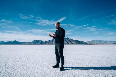 Ciddi boncuklu erkek kaşifin tam kenar görüntüsü günlük kıyafetleriyle modern tabletleri karıştırıyor Amerika 'da kayalarla çevrili.
