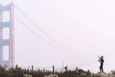 San Francisco 'da Golden Gate Köprüsü yakınlarında elinde tabletle VR gözlüklerini araştıran tanınmayan bir kadının yan görüntüsü.