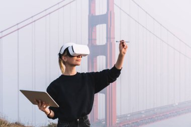 Beyaz VR kulaklıklı, ciddi bir kadın. Şehirdeki sanal ekranda Stylus 'lu grafik tabletle bakıyor ve çiziyor.