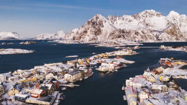 Geleneksel kırmızı Norveç evleriyle Lofoten balıkçı köyünün nefes kesici kuş bakışı görüntüsü. Fiyort arasında küçük şehir altyapısı olan panoramik ada manzarasının insansız hava aracı görüntüsü