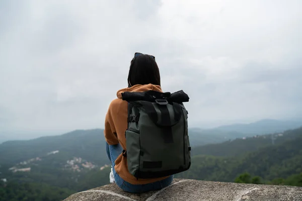 Back view of female traveler with backpack resting on sightseeing tour explore location on journey, woman tourist looking at landscape on wanderlust journey sitting on destination for discover