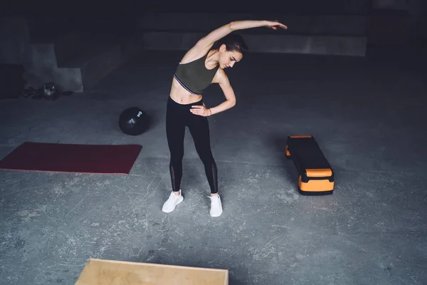 身穿运动服的强壮年轻女子穿着灰色运动服在健身房进行侧弯伸展运动 — 图库照片