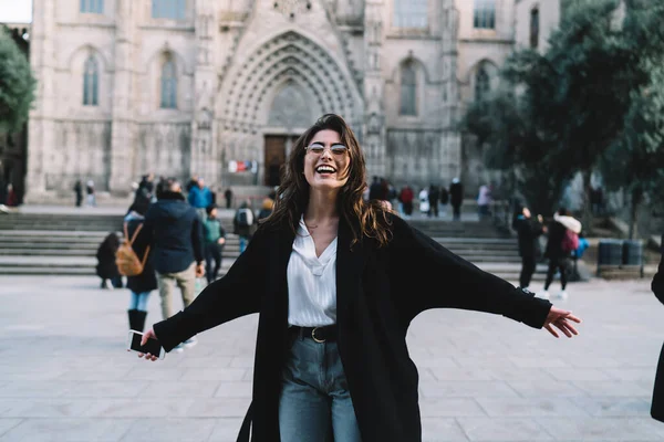 Half length portrait of cheerful female tourist with modern mobile satisfied with time for exploring historic places, carefree woman smiling at camera feeling freedom at Italian square with duomo