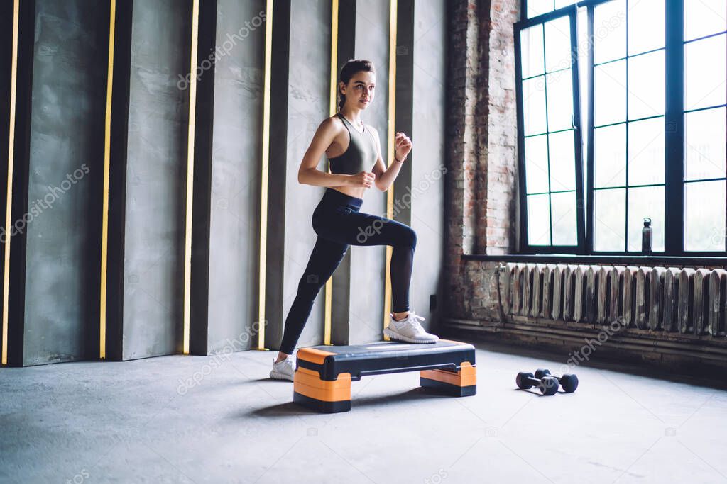 Determined slim caucasian female doing steps exercising using gym equipment keeping perfect body shape, serious 20s woman spending time on healthy lifestyle and workout for muscular strength