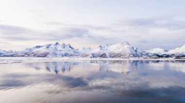Norveç deniz suyuna yansıyan beyaz karla kaplı yüksek dağlı kayalık tepelerin nefes kesici kuş bakışı görüntüsü. Kışın Lofoten 'in nefes kesici panoramik fiyortları, doğanın sakin güzelliği. 