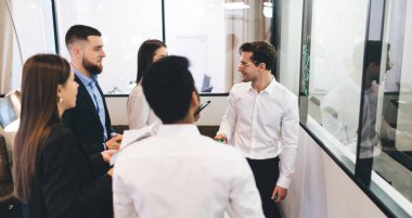 Yüksek açılı başarılı iş ortakları klas resmi kıyafet modern ofiste duruyor ve proje detaylarını tartışıyor