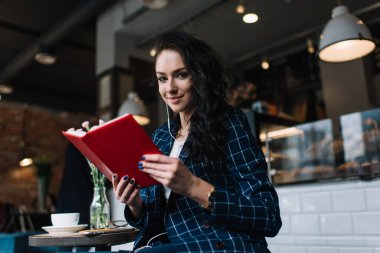 Resmi giyinmiş, ahşap masada oturmuş, elinde kitap tutarak müzik dinleyen neşeli kadının alçak açısı.