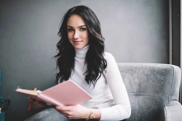 积极的女企业家穿着休闲装 坐在舒适的扶手椅上 带着粉红笔记本 一边看着相机一边想着生意 — 图库照片