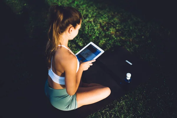 緑の芝生の上に座ってスポーツウェアで若い女性の側のビューからと晴れた夏の日にタブレット上でサーフィンインターネット — ストック写真